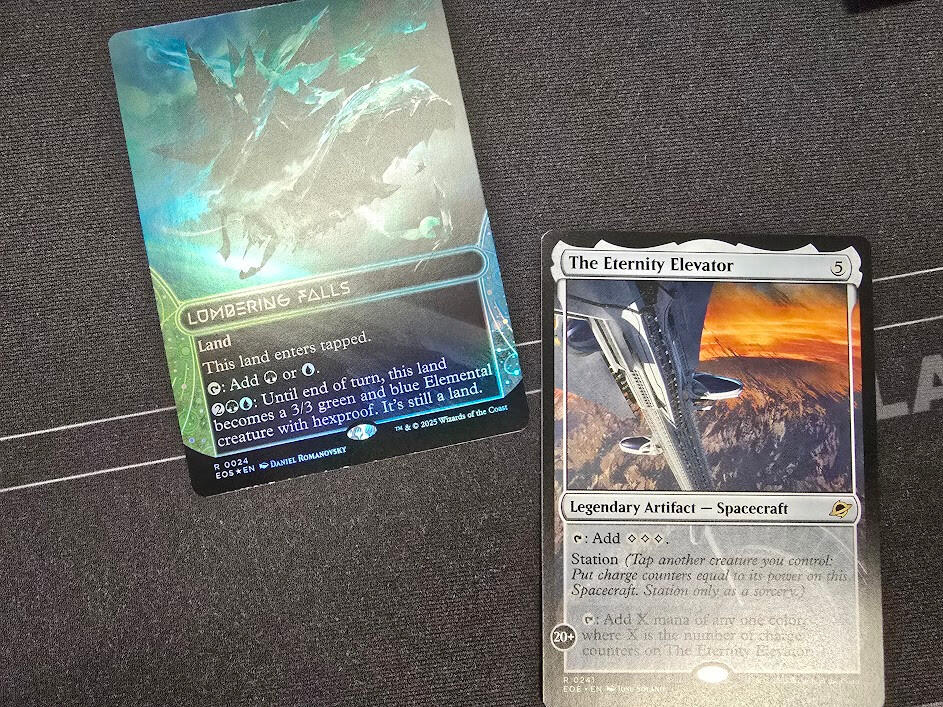 Two Magic the Gathering cards on a playmat. One is Lumbering Falls, a land card. The other is The Eternity Elevator, a Legendary Artifact (Spacecraft).